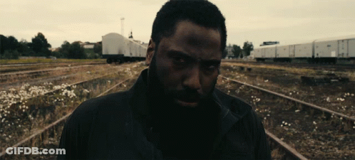 A Man With A Beard Is Standing In A Train Yard GIF