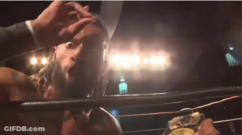 A Man With A Beard Is Standing In A Wrestling Ring Holding A Championship Belt . GIF