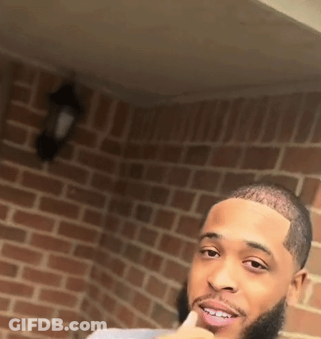 A Man With A Beard Is Standing In Front Of A Brick Wall . GIF