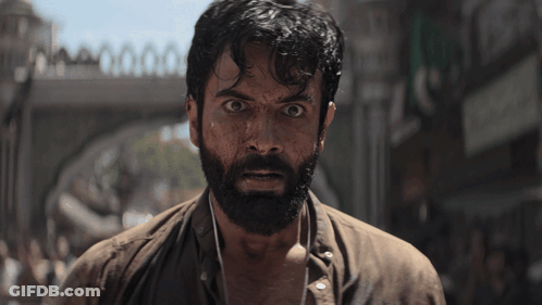A Man With A Beard Is Standing In Front Of A Bridge GIF