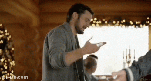 A Man With A Beard Is Standing In Front Of A Christmas Tree In A Cabin . GIF