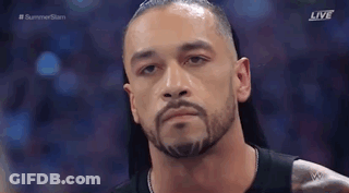 A Man With A Beard Is Standing In Front Of A Crowd And Looking At The Camera . GIF