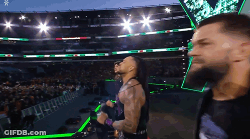 A Man With A Beard Is Standing In Front Of A Crowd In A Stadium With Green Lights GIF