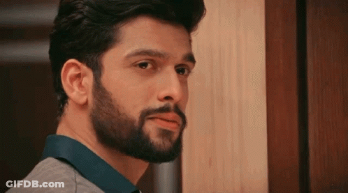 A Man With A Beard Is Standing In Front Of A Door GIF