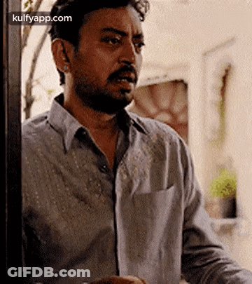 A Man With A Beard Is Standing In Front Of A Door And Looking Out . GIF