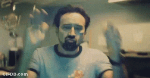 A Man With A Beard Is Standing In Front Of A Glass Door With His Hands Behind It . GIF