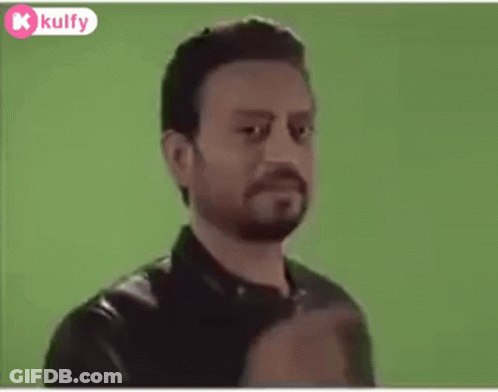 A Man With A Beard Is Standing In Front Of A Green Screen And Looking At The Camera . GIF
