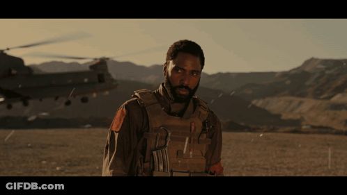A Man With A Beard Is Standing In Front Of A Helicopter And Mountains GIF