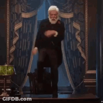 A Man With A Beard Is Standing In Front Of A Lamp In A Room . GIF