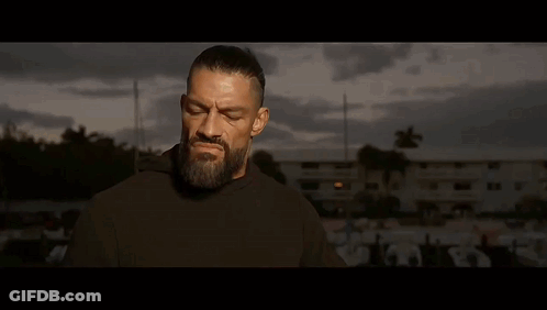 A Man With A Beard Is Standing In Front Of A Man With His Hands Folded . GIF