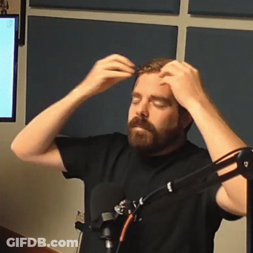 A Man With A Beard Is Standing In Front Of A Microphone And Adjusting His Hair GIF