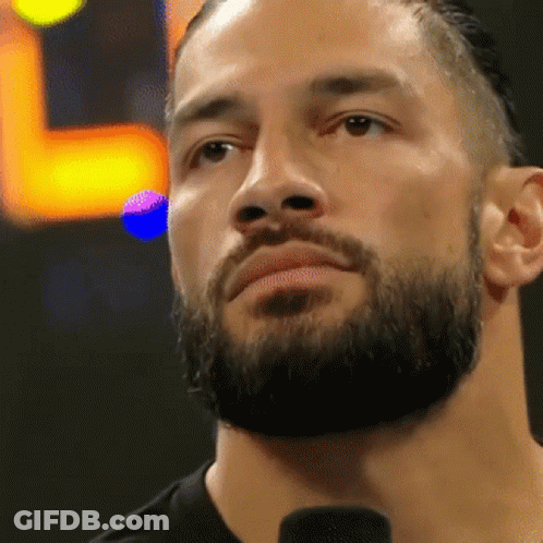 A Man With A Beard Is Standing In Front Of A Microphone And Looking At The Camera . GIF