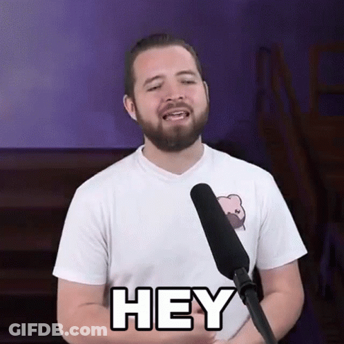 A Man With A Beard Is Standing In Front Of A Microphone And Saying Hey . GIF