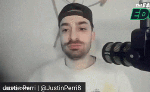 A Man With A Beard Is Standing In Front Of A Microphone And Talking Into It . GIF