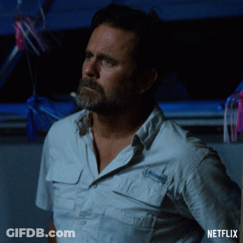 A Man With A Beard Is Standing In Front Of A Netflix Sign GIF