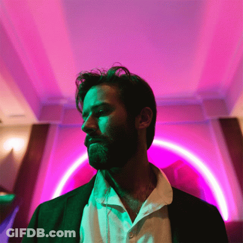 A Man With A Beard Is Standing In Front Of A Purple And Green Light GIF