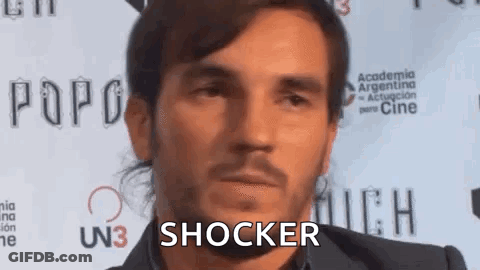 A Man With A Beard Is Standing In Front Of A Red Carpet . GIF