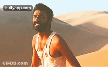 A Man With A Beard Is Standing In Front Of A Sand Dune In The Desert . GIF
