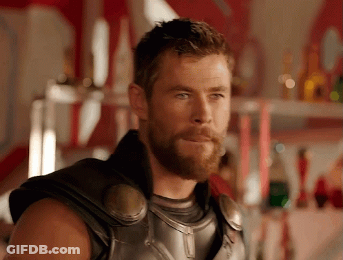 A Man With A Beard Is Standing In Front Of A Shelf With Bottles On It GIF