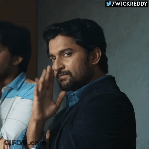A Man With A Beard Is Standing In Front Of A Sign That Says ' 7Wickreddy ' On It GIF