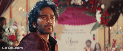A Man With A Beard Is Standing In Front Of A Sign That Says ' Ayaan ' On It GIF