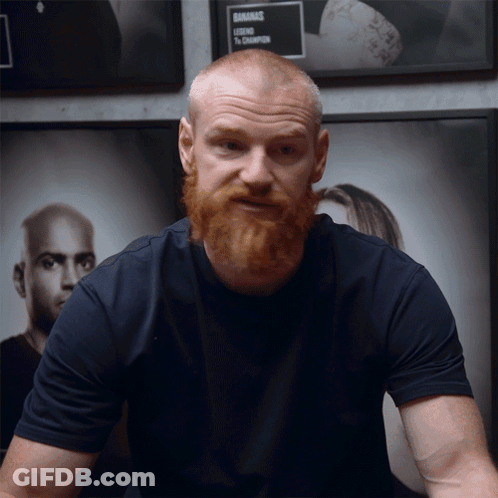 A Man With A Beard Is Standing In Front Of A Sign That Says ' Gnarmac ' On It GIF