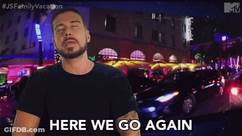 A Man With A Beard Is Standing In Front Of A Sign That Says Here We Go Again GIF