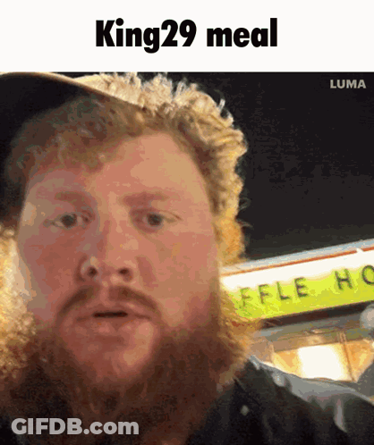 A Man With A Beard Is Standing In Front Of A Sign That Says King 29 Meal GIF