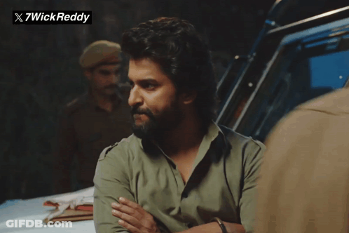 A Man With A Beard Is Standing In Front Of A Sign That Says X7wickreddy GIF