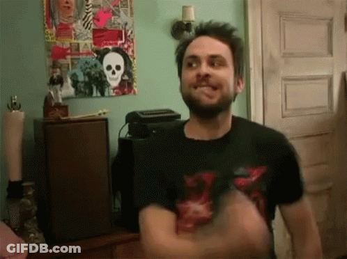 A Man With A Beard Is Standing In Front Of A Skull Poster On The Wall GIF