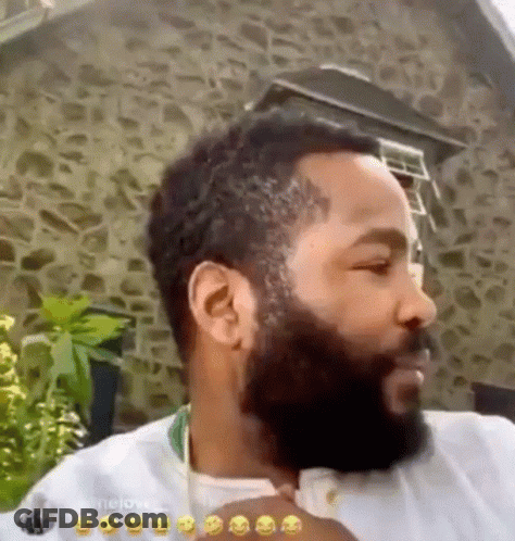 A Man With A Beard Is Standing In Front Of A Stone Building And Making A Funny Face . GIF