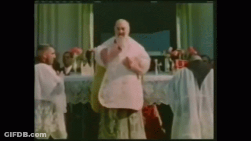 A Man With A Beard Is Standing In Front Of A Table With Flowers On It GIF