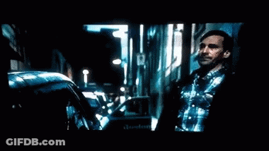 A Man With A Beard Is Standing In Front Of A Television Screen . GIF