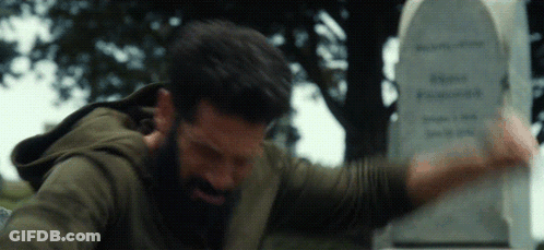 A Man With A Beard Is Standing In Front Of A Tombstone GIF