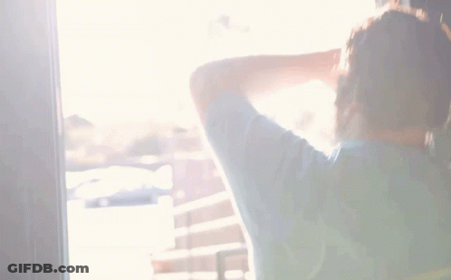 A Man With A Beard Is Standing In Front Of A Wall And Covering His Face With His Hand GIF