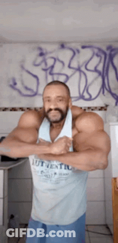 A Man With A Beard Is Standing In Front Of A Wall With Graffiti . GIF
