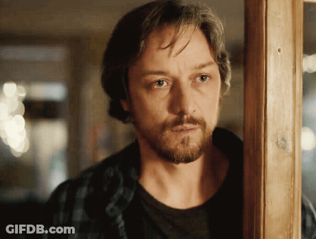 A Man With A Beard Is Standing In Front Of A Wooden Door GIF