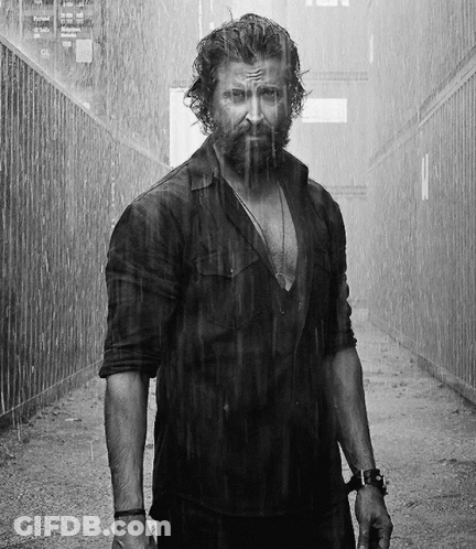A Man With A Beard Is Standing In The Rain Looking At The Camera GIF