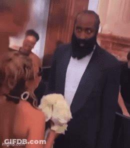 A Man With A Beard Is Standing Next To A Woman In A Wedding Dress . GIF