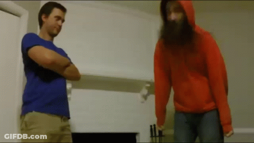 A Man With A Beard Is Standing Next To A Woman In An Orange Hoodie GIF