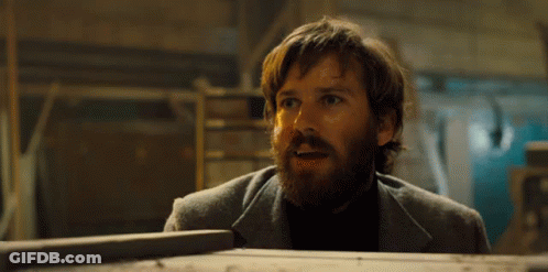 A Man With A Beard Is Standing Next To A Wooden Box And Making A Surprised Face . GIF