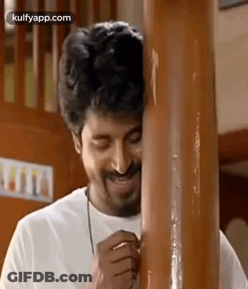 A Man With A Beard Is Standing Next To A Wooden Pole And Smiling . GIF