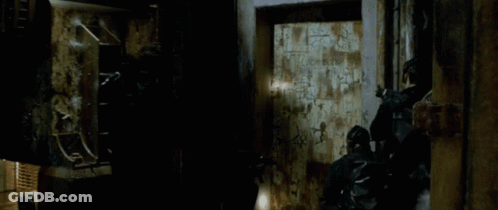 A Man With A Beard Is Standing Next To Another Man In A Dark Room . GIF