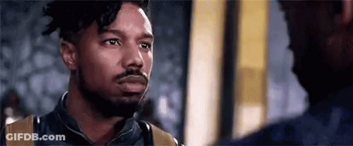 A Man With A Beard Is Standing Next To Another Man In A Room . GIF