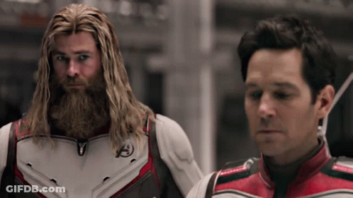 A Man With A Beard Is Standing Next To Another Man With Long Hair . GIF