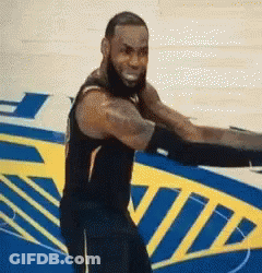 A Man With A Beard Is Standing On A Basketball Court In Front Of A Sign That Says ' Nba ' . GIF