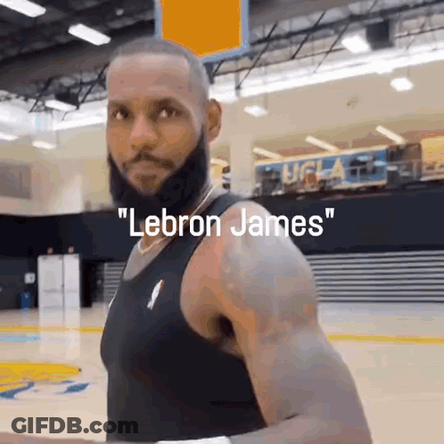 A Man With A Beard Is Standing On A Basketball Court With The Words Lebron James Written Above Him . GIF