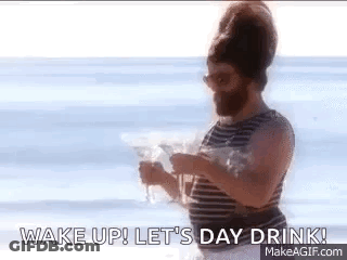A Man With A Beard Is Standing On A Beach Holding A Drink . GIF