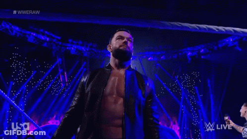 A Man With A Beard Is Standing On A Stage In Front Of A Crowd While Wearing A Black Jacket . GIF
