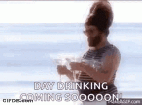 A Man With A Beard Is Standing On The Beach Drinking A Glass Of Wine . GIF